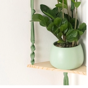 Dettaglio di mensola a muro in macramè nordico con corda intrecciata verde e base in legno
