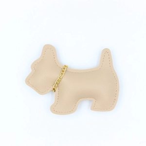 Close-up of beige lychee texture leather Scottie dog charm with gold chain detail