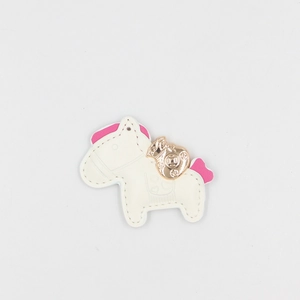 Detailed close-up of a white leather pony keychain with gold lucky bag and pink accents