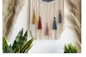 Close-up of macrame wall hanging with colorful tassels and wooden beads on white wall