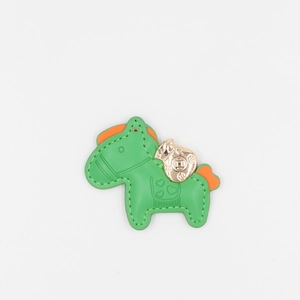 Close-up of green leather horse charm with gold money bag detail and orange accents