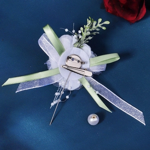 Detail of white fabric wedding corsage with green ribbons and dual metal clip back