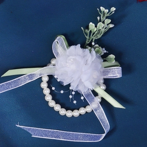 Detail of a white tulle wedding wrist corsage with artificial pearls and green leaf accents