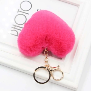 Pink heart plush keychain with golden metal ring on a white decorative frame