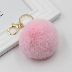 Detail of a soft pink faux rabbit fur pompom keychain with golden metal clasp