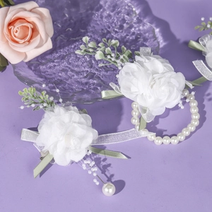 Detailed view of white satin rose corsage and wrist flower with pearls and green ribbons