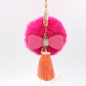Detail of plush pompom keychain with pink bow, orange tassel, and golden hardware