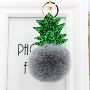 Détail d'un porte-clés pompon ananas gris avec feuilles pailletées vertes et or