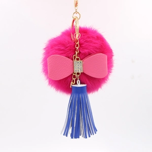 Close-up of pink faux fur ball keychain with leather bow, blue tassel and gold metal link