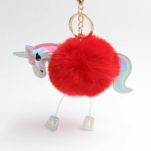 Close-up of fluffy red unicorn pompom keychain with holographic details and gold hardware