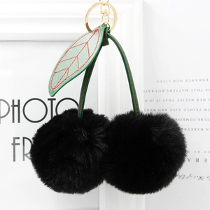 Close-up of plush cherry keychain with black faux fur balls and green leather leaves