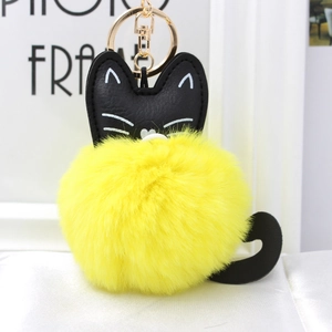 Close-up of cute cat keychain featuring a bright yellow fluffy pompom and black faux leather