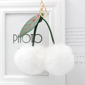 Detail of white faux fur cherry keychain with green leather leaves and gold hardware