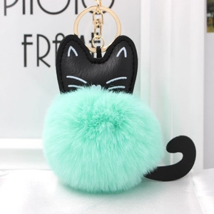 Close-up of fluffy green pompom cat keychain with black ears and golden metal clasp