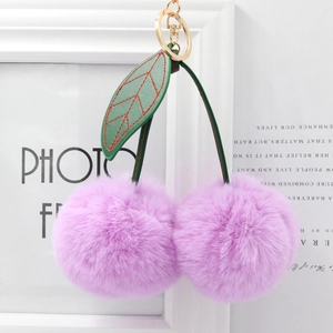 Detail of purple faux fur cherry pom-poms with green leather leaves and gold keychain ring