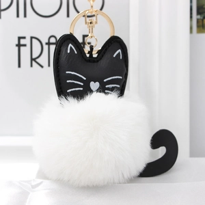 Close-up of cat keychain with white faux fur ball and gold metal clasp on satin base