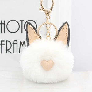 Détail d'un pompon chat blanc en peluche avec oreilles en cuir et porte-clé doré brillant