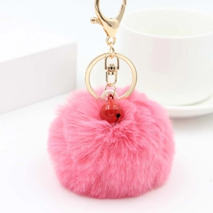 Nahaufnahme von flauschigem rosa Kunstfell-Bommel-Schlüsselanhänger mit roter Glocke