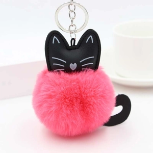 Close-up of pink fluffy cat pompom keychain with black leather details on a white table