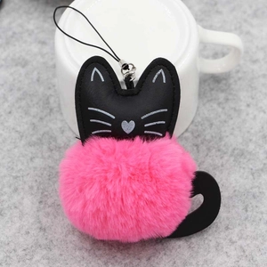 Détail du porte-clés chat en peluche avec boule rose et tête en cuir sur une tasse blanche