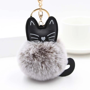 Close-up of fluffy grey and white cat keychain with gold metal ring and leather cat head