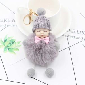 Close-up of sleeping baby plush keychain with grey pom-pom and pink bow detail