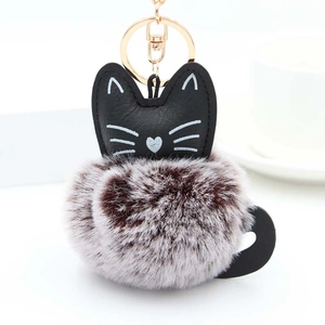 Detail of cute cat keychain featuring a black faux leather head and fluffy bicolor pom pom