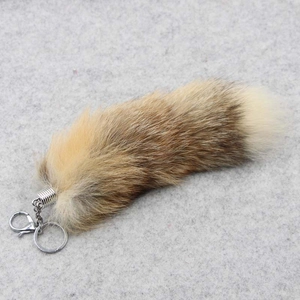 Detail of a large fluffy fox tail keychain with metal ring on a grey felt surface