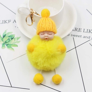 Detail of yellow plush sleeping baby keychain with knit hat and soft pompom on desk
