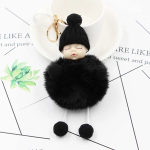 Close-up of sleeping baby plush keychain with black faux fur pompom and knitted hat