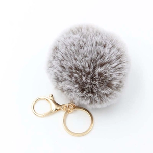 Detailed view of the soft brown and grey faux fur pom pom with gold lobster clasp hook