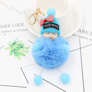 Dettaglio portachiavi pompon azzurro con bambola che dorme e fiocco decorativo rosso