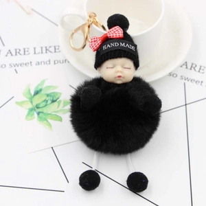 Dettaglio portachiavi con bambola che dorme, pompon nero e fiocco su cappello a maglia