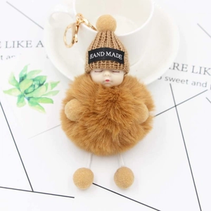 Detail of a brown plush sleeping baby keychain with a knitted hat and golden hardware