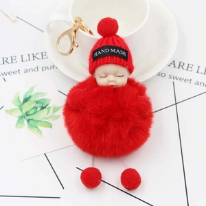 Detail of red sleeping baby plush doll keychain with handmade hat beside a white cup