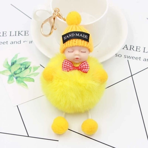 Détail porte-clés pompon jaune avec bébé endormi et décoration de nœud à carreaux