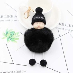 Close-up of a sleeping baby plush keychain with black faux fur pompom and gold hook