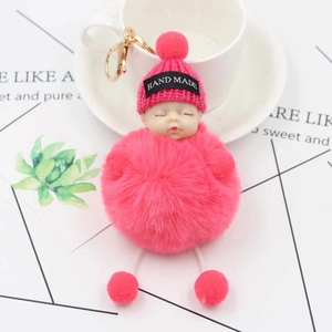 Pink sleeping baby plush keychain with gold carabiner on a decorative background