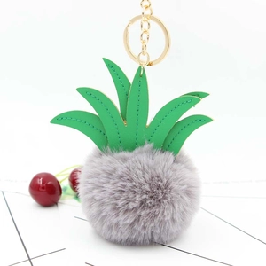 Detailed view of grey faux fur pineapple keychain with green PU leaves and gold metal clip