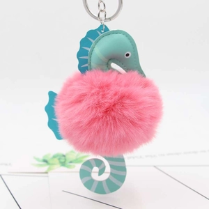 Macro detail of seahorse keychain with pink plush pompom and blue faux leather accents