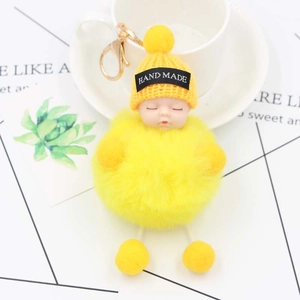 Close-up of yellow sleeping baby doll keychain with plush pom-poms and gold clasp