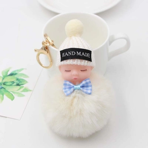Détail d'un porte-clés poupée endormie avec pompon en peluche beige et attache dorée