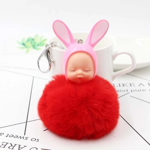 Close-up of a red fluffy pom-pom keychain with a sleeping baby doll and pink rabbit ears