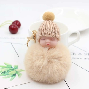 Portachiavi con bambola neonato beige, pompon di peluche e cappello in maglia