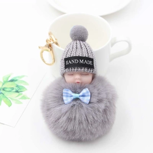 Détail d'un porte-clés poupée endormie en peluche avec bonnet gris et nœud bleu