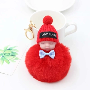 Détail d'un porte-clés bébé endormi en peluche avec pompon rouge et fermoir mousqueton doré