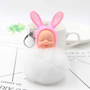 Close-up of fluffy white pom-pom keychain with pink rabbit ears and sleeping baby doll