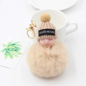 Détail d'un porte-clés bébé endormi fait main avec pompon beige et bonnet en maille douce