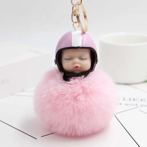 Close-up of pink fluffy pompom keychain with a cute helmet baby doll and golden metal clasp