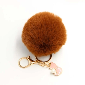 Close-up of fluffy tan pompom keychain with pink cat charm and pearl detail